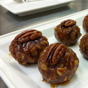 Pecan Pie Balls You’ll Fall in Love With 5 A close-up image of Pecan Pie Balls topped with a whole pecan and coated in syrup, arranged on a white plate.