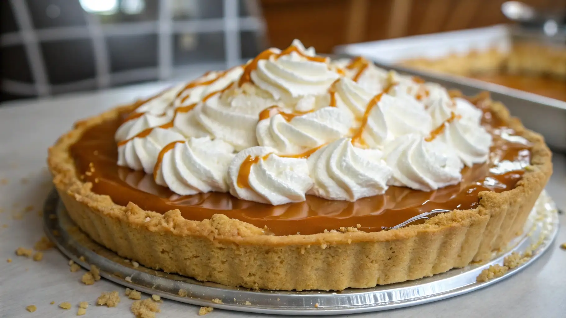 A close-up of a delicious Caramel Cream Pie with a golden graham cracker crust, topped with whipped cream swirls and drizzled with caramel.
