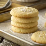 Stack of golden 3 ingredient sugar cookies on a parchment-lined baking tray, topped with coarse sugar.