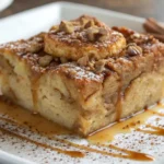 A close-up shot of a delicious gluten-free bread pudding with caramel sauce, powdered sugar, and chopped nuts on top.