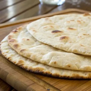 Freshly cooked unleavened bread stacked on a wooden cutting board.