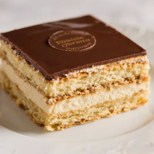 Slice of classic French Opera cake with layers of almond sponge, coffee buttercream, ganache, and glossy chocolate glaze on a white plate.