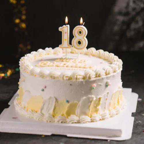 White frosted 18th birthday cake decorated with candles shaped like number 18 and colorful sprinkles on top for a celebration.