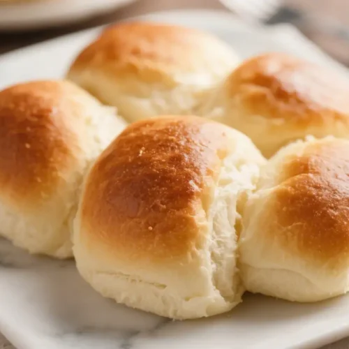 Freshly baked dinner rolls with golden tops and soft fluffy texture on a plate