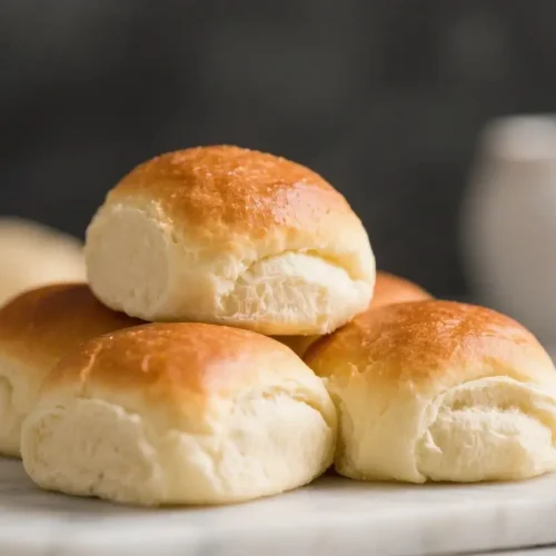 Soft golden Parker House rolls stacked on a marble board showing fluffy interior texture and lightly browned tops
