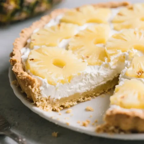 Tropical Pineapple Cream Pie (Easy Crowd-Pleaser) - Bright, Creamy, and Refreshing 2 Pineapple cream pie with a buttery crust and fluffy whipped cream filling, topped with pineapple rings, with a slice removed on a white plate.