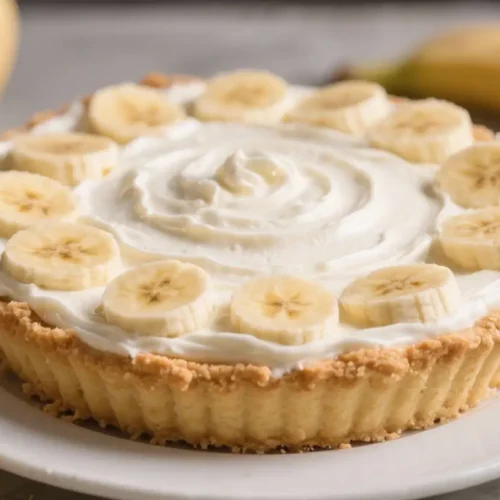 Banana cream pie topped with fresh banana slices and smooth whipped cream on a buttery crust.