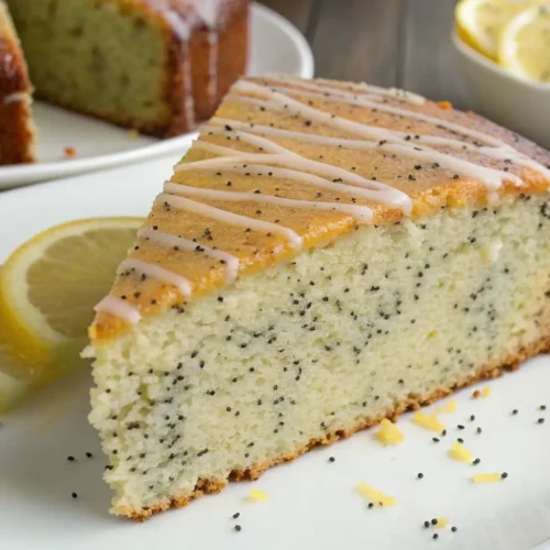 Moist Lemon Poppy Seed Cake (Easy Glazed Recipe) - Bright, Tender, and Foolproof 2 Slice of lemon poppy seed cake with a light lemon glaze drizzle on a white plate, served with fresh lemon slices and extra poppy seeds.
