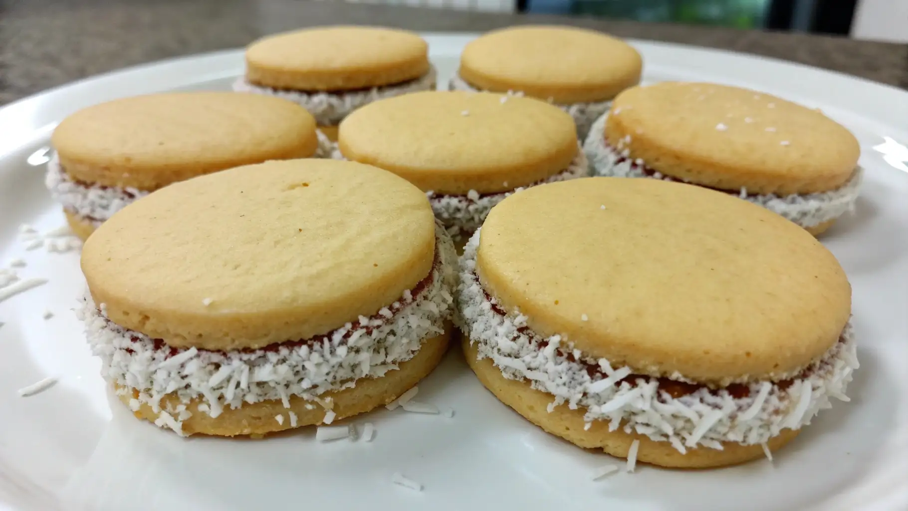 Homemade alfajores cookies filled with dulce de leche and rolled in shredded coconut on a white plate