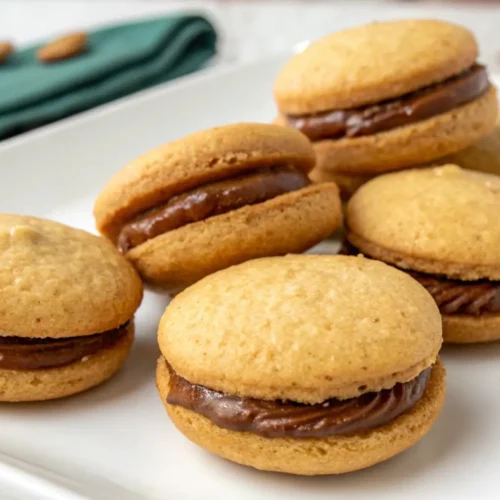 Baci di Dama Italian Hazelnut Sandwich Cookies – Crisp, Buttery, and Chocolate-Filled 2 Baci di Dama Italian hazelnut sandwich cookies filled with chocolate cream on a white platter