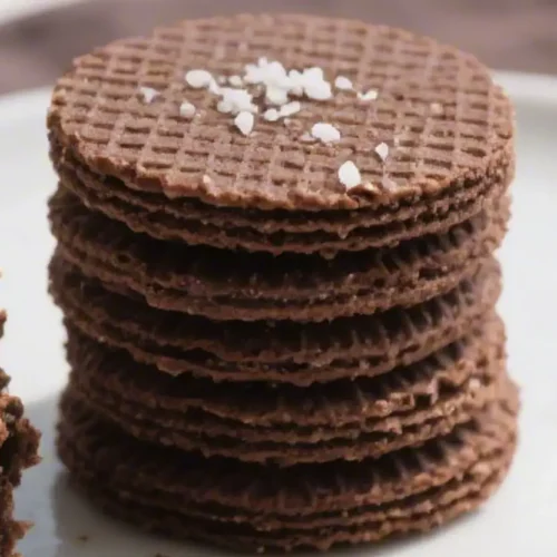 Stack of thin chocolate wafer cookies with a crisp waffle pattern on a white plate.