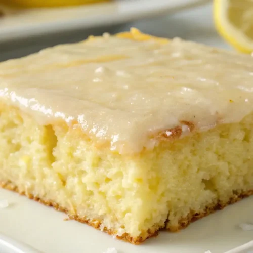 Lemon Buttermilk Sheet Cake Soft Moist Easy Homemade Dessert - Bright, Tender, and Crowd-Friendly 2 Moist lemon buttermilk sheet cake with creamy lemon glaze on top, served on a plate with fresh lemon slices