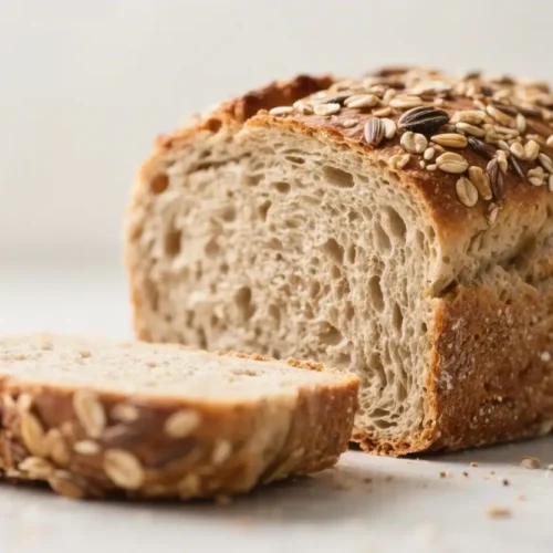 Sliced loaf of multigrain bread topped with mixed seeds on a neutral surface.
