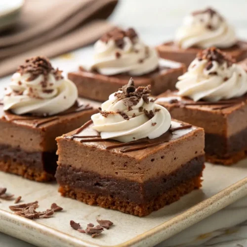 French silk pie brownies with layered chocolate base, creamy mousse topping, and whipped cream swirls garnished with chocolate shavings on a serving plate