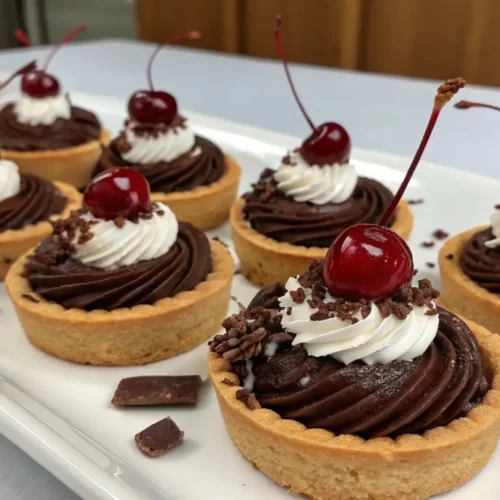 Mini Black Forest Mousse Tarts Easy Chocolate Cherry Dessert - A Quick, Crowd-Pleasing Treat 2 Mini Black Forest mousse tarts with chocolate ganache filling whipped cream topping and fresh cherries served on a white platter