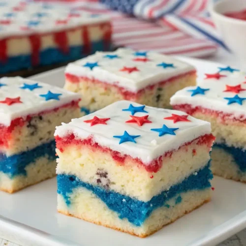 Patriotic poke cake squares with red white and blue layers topped with white frosting and star sprinkles on a serving plate