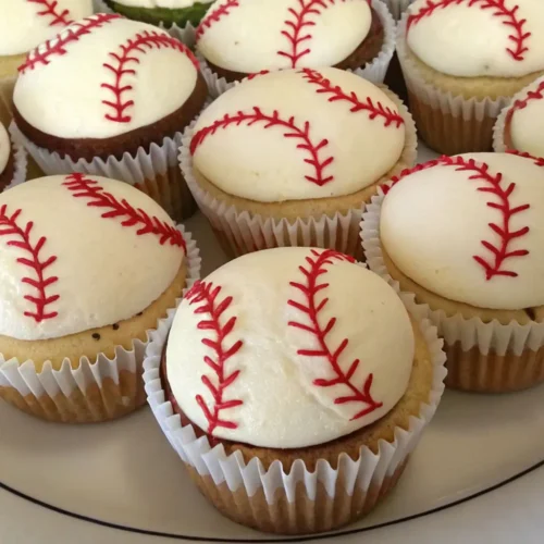 Easy Baseball Cupcakes for Game Day Party Dessert - Fun, Festive, and Fast 2 Baseball-themed cupcakes with smooth white frosting and red stitched icing, arranged on a white plate, resembling miniature baseballs.