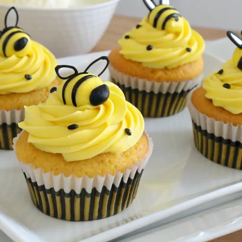 Bee cupcakes decorated with yellow frosting, black stripes, and cute bee toppers on vanilla cupcakes displayed on a white tray