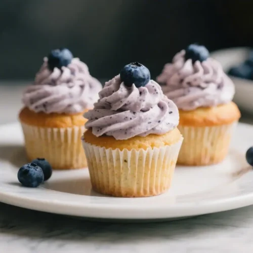 Blueberry cupcakes with purple blueberry frosting topped with fresh blueberries on a white plate