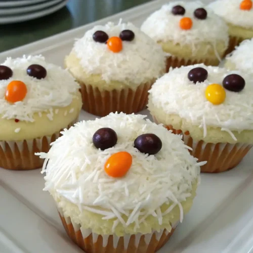 Cute Chicken Cupcakes Recipe for Parties and Kids Snacks - Fun, Easy, and Adorable 2 Cute chicken cupcakes decorated with white coconut frosting, candy eyes, and orange candy beaks arranged on a white plate for a fun party dessert