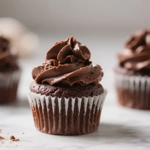 Chocolate cupcake in a paper liner on a white surface with chocolate pieces nearby, partially covered by a glitch or overlay effect.