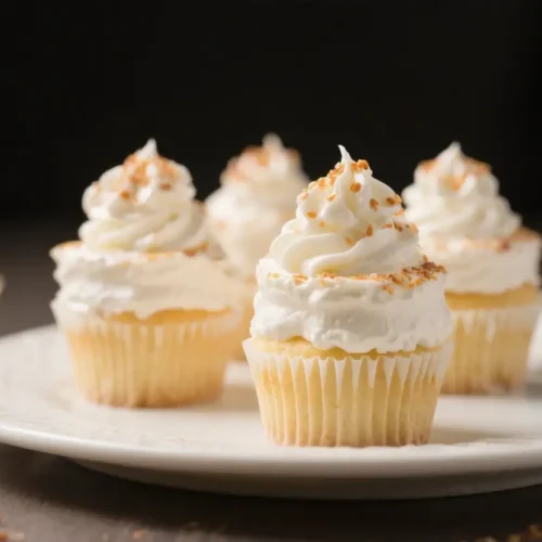 Tres leches cupcakes topped with whipped cream frosting and sprinkled crumbs served on a white plate.
