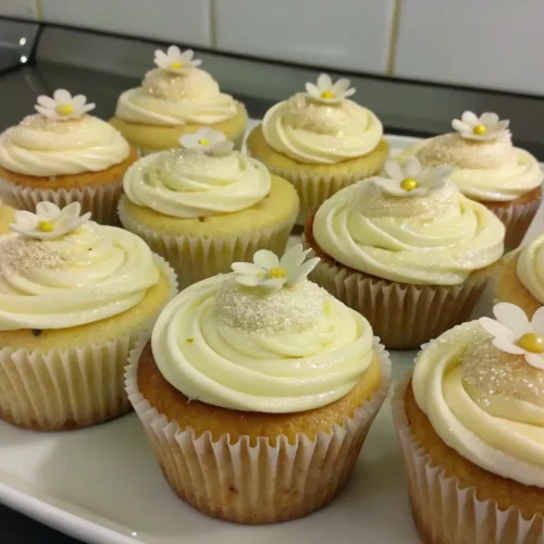 Easy Vanilla Cupcakes Recipe for Beginners – Simple, Soft, and Foolproof 2 Vanilla cupcakes with creamy buttercream frosting and small flower decorations on a serving plate