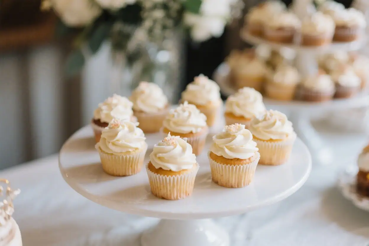 Elegant wedding cupcakes with vanilla frosting displayed on a white cake stand at a wedding dessert table