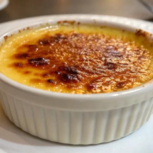 Crème Brûlée Recipe with a Perfect Caramelized Sugar Top – Simple, Silky, and Classic 2 Classic crème brûlée in a white ramekin with a golden caramelized sugar crust, served on a white plate.