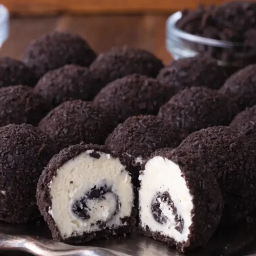 Oreo cheesecake truffles coated in crushed chocolate cookie crumbs, with one truffle cut open to show a creamy cookies-and-cream center.